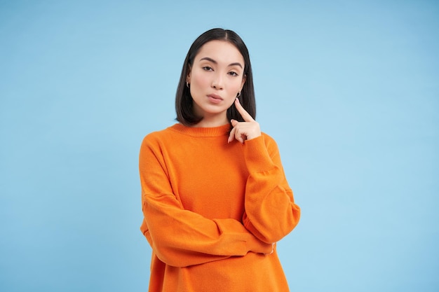 Free photo thoughtful asian woman looking with interest at camera thinking smth making decision standing over b