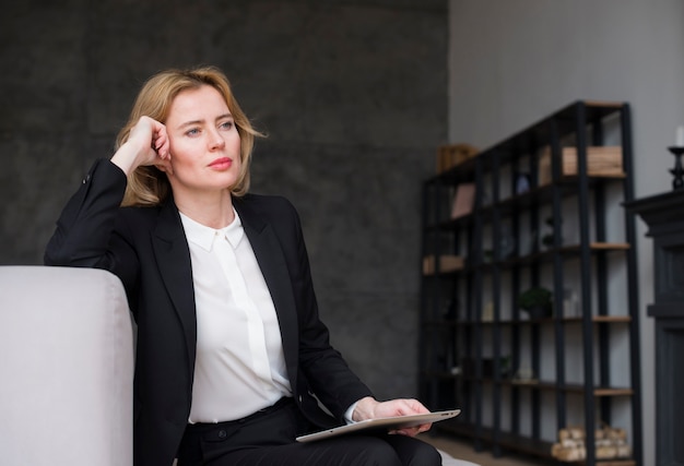 Thoughtful blond business woman in suit with tablet