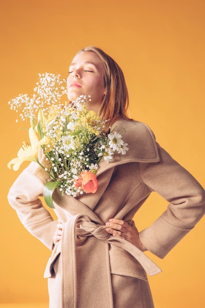 Free photo thoughtful blond woman with flowers bouquet in coat