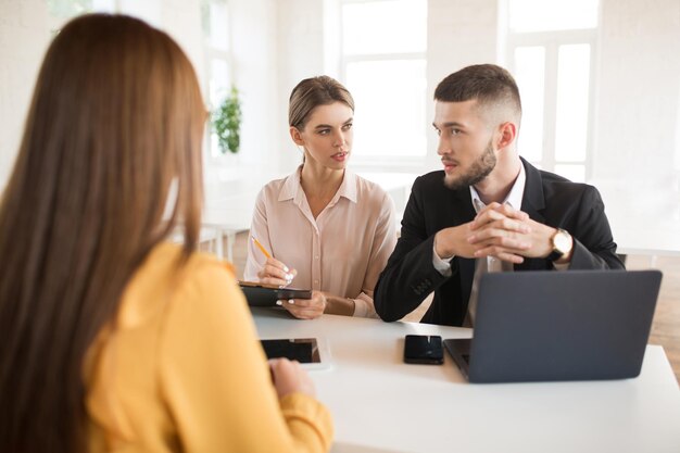 Thoughtful business man with laptop and business woman with pencil and folder in hands thoughtfully consulting together about applicant Young employers spending job interview in modern office