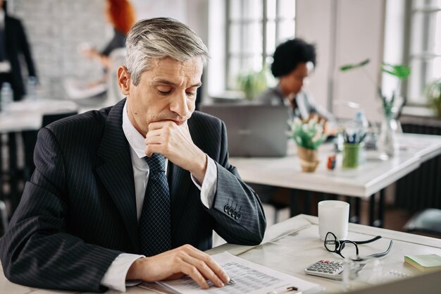 Thoughtful businessman sitting at desk in the office and going through financial reports