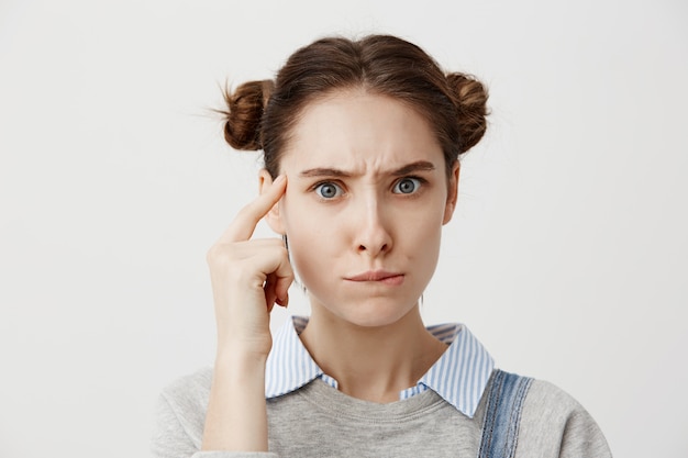 Free photo thoughtful caucasian woman in casual holding finger at her temple posing with meaningful look. young female having confused pensive emotions pondering about her lifestyle