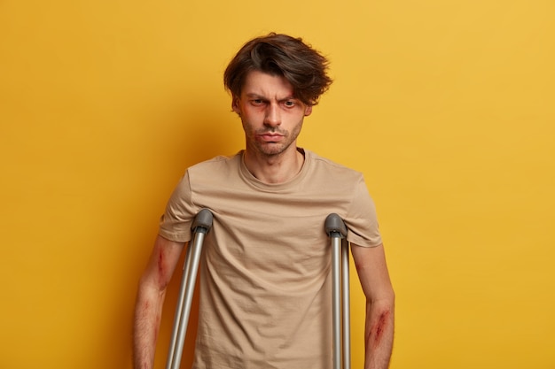 Free Photo thoughtful dissatisfied man with bruises around eyes has life threating injury, feels terrible pain, recovers after surgery at home, isolated over yellow wall, suffers after road traffic accident