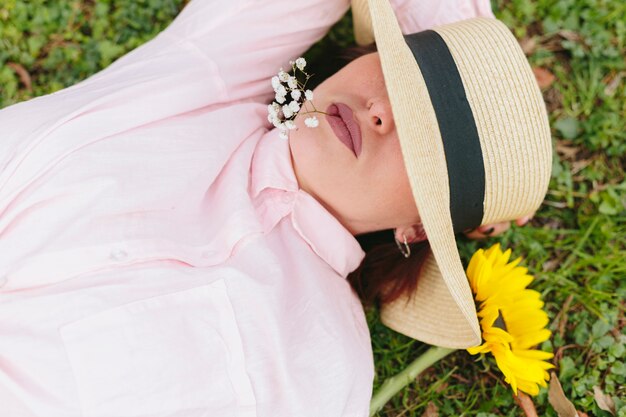 Thoughtful female in hat lying on grass