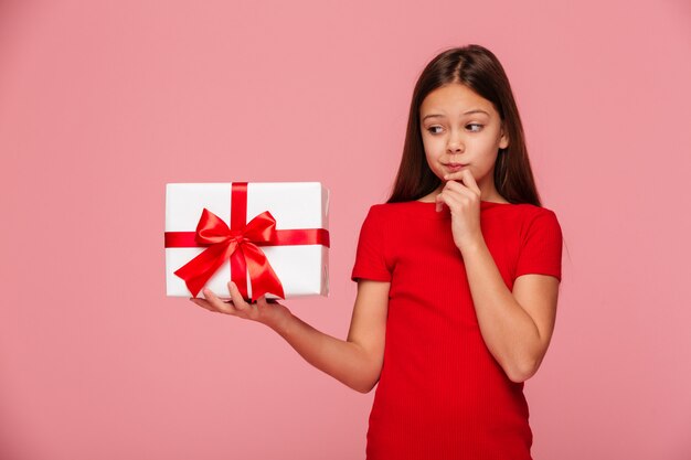 Thoughtful girl looking at gift on hand and thinking about it isolated