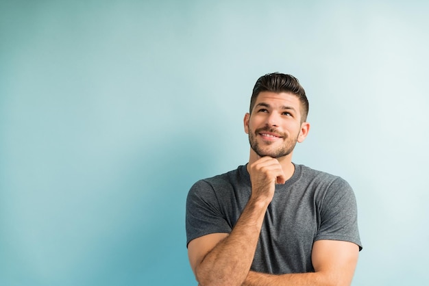 Thoughtful good looking young man looking up while smiling in studio