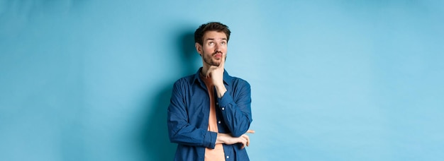 Free Photo thoughtful handsome guy making plan looking up pensive imaging things standing on blue background