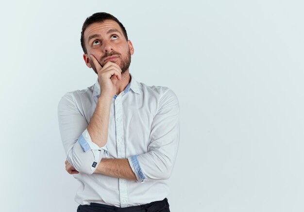 Thoughtful handsome man puts hand on chin looking up isolated on white wall