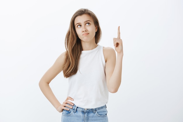 Thoughtful and indecisive attractive girl pointing and looking up