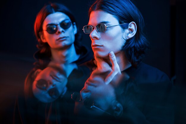 Thoughtful look. Portrait of twin brothers. Studio shot in dark studio with neon light