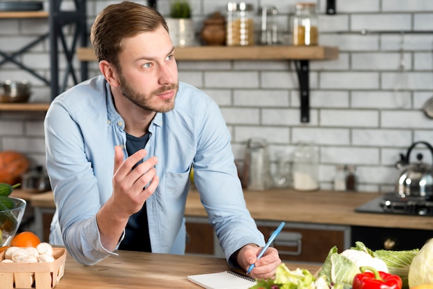 Thoughtful man writing recipe in kitchen