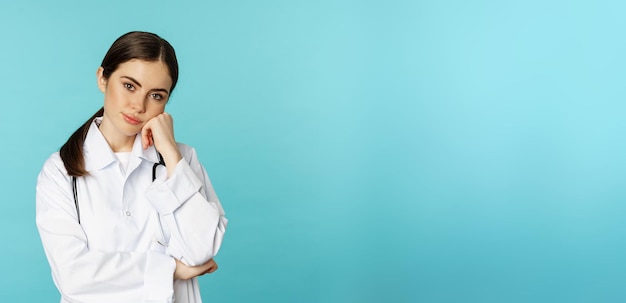 Thoughtful medical worker young doctor woman looking unamused bored standing in white coat against b