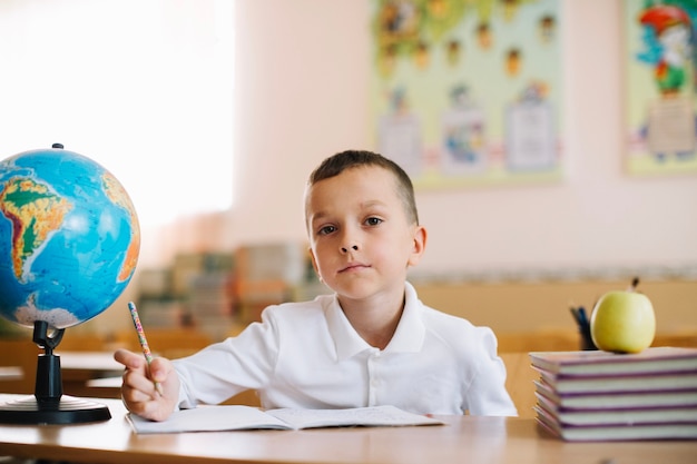 Thoughtful pupil with globe on desk