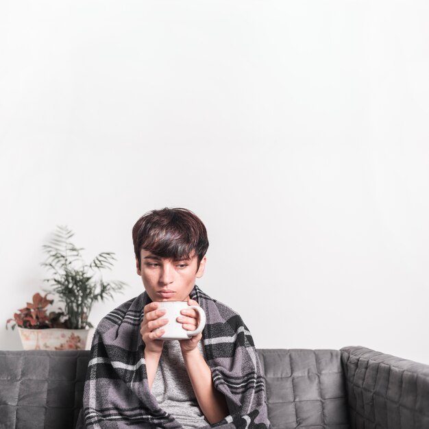 Thoughtful sick woman with blanket holding coffee mug