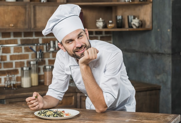 Free photo thoughtful smiling male chef leaning on the counter with a dish in the kitchen