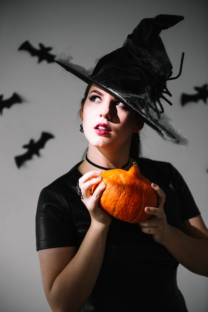 Thoughtful witch with pumpkin looking up