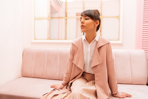 Free Photo thoughtful woman in coat sitting on a sofa in cafe