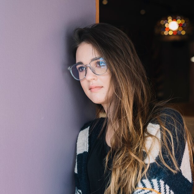 Thoughtful woman in glasses standing at wall