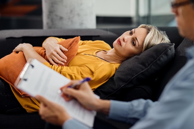 Free Photo thoughtful woman lying down on psychiatrist's couch during an appointment with her therapist