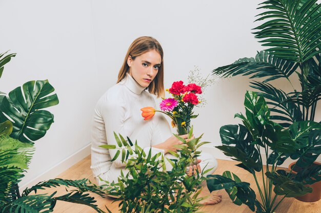 Thoughtful woman sitting with flowers near green plants 