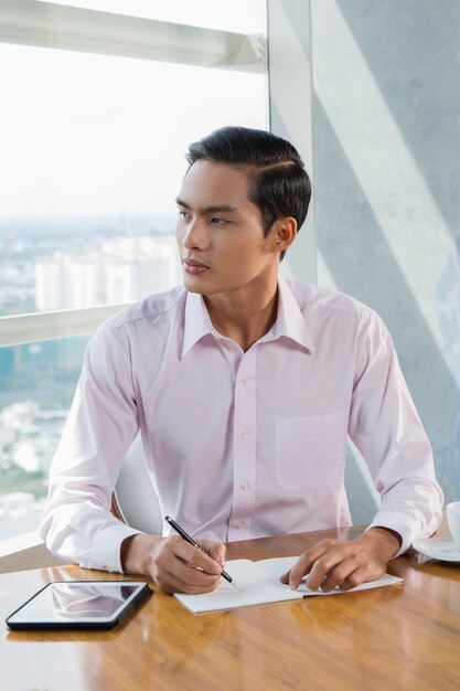 Thoughtful Young Asian Man Working in Cafe