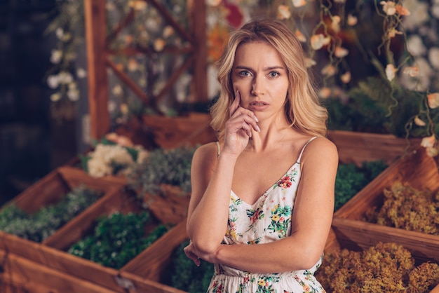 Free photo thoughtful young blonde woman in floral dress standing in front of wooden crate