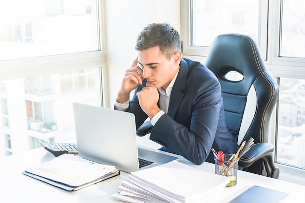 Thoughtful young businessman looking at laptop at workplace