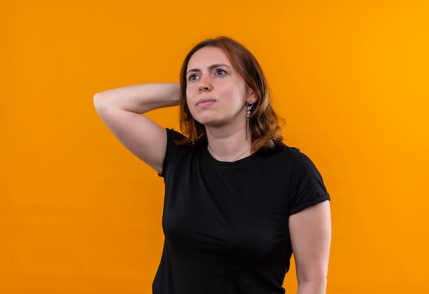 Thoughtful young casual woman putting hand behind head on isolated orange wall