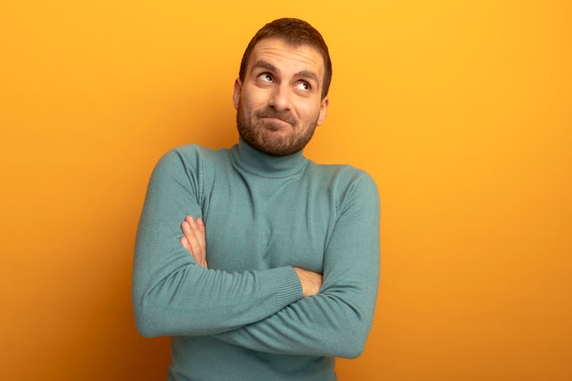 Free Photo thoughtful young caucasian man standing with closed posture looking at side isolated on orange background with copy space