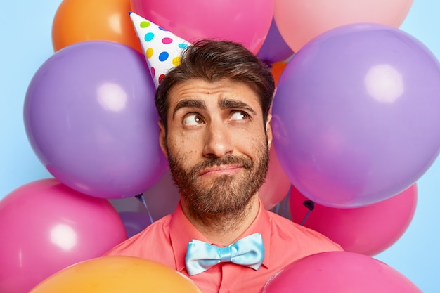 Thoughtful young guy posing surrounded by birthday colorful balloons