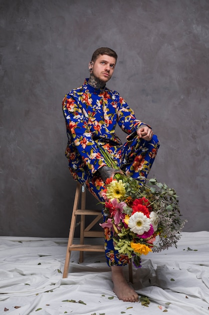 Free photo thoughtful young man sitting on wooden small ladder holding flower bouquet in hand