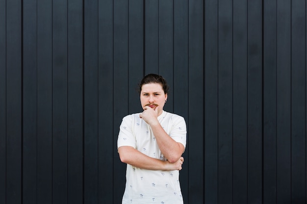 Free photo thoughtful young man with his hand on chin standing against black striped wall