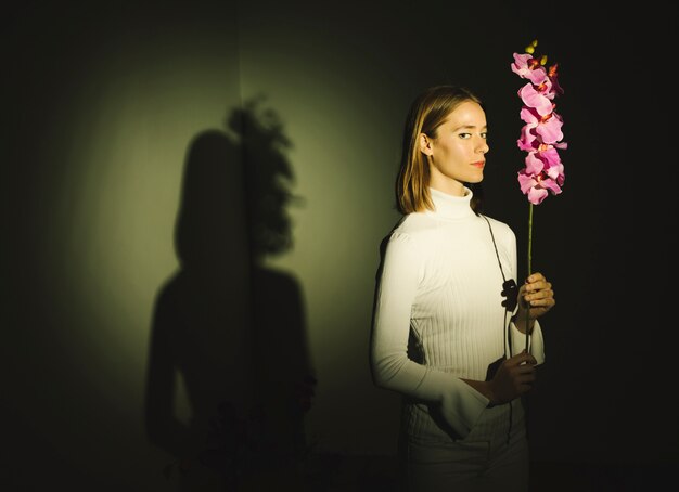 Thoughtful young woman holding bright flower 