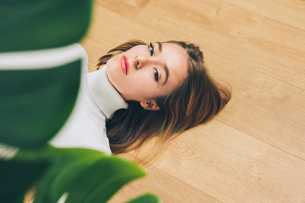 Free photo thoughtful young woman lying on floor near plant