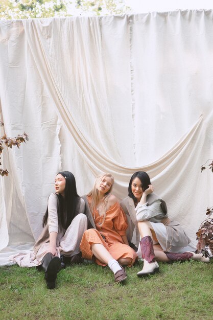 Three beautiful women sitting on the ground and smiling in garden .