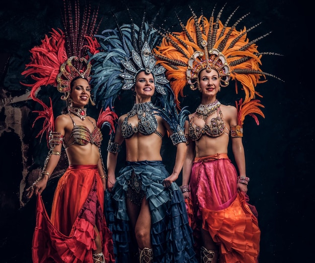 Free photo three beautiful young womans in traditional brasilian carnaval costumes are posing for photographer at studio.