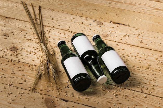 Free photo three beer bottles and ears of wheat on wooden background