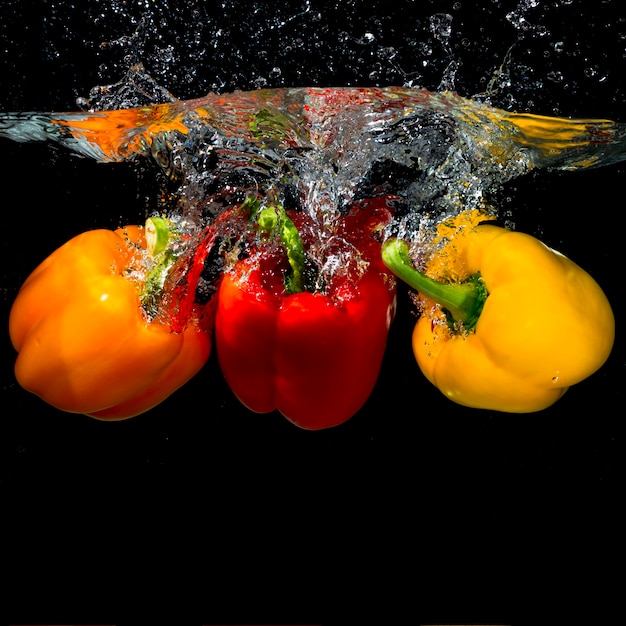 Three bell peppers falling into the splash water