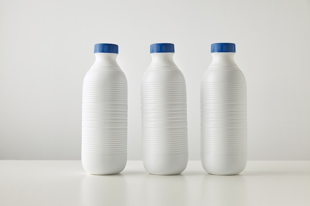 Three blank white plastic riffled bottles with blue caps in row isolated on table in center