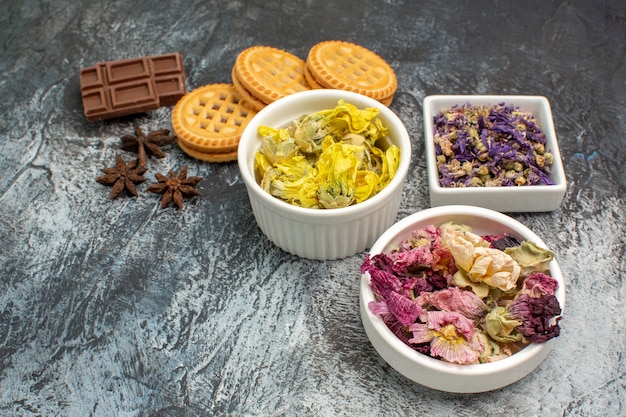 Free photo three bowls of dry flowers with chocolate and cookies on grey