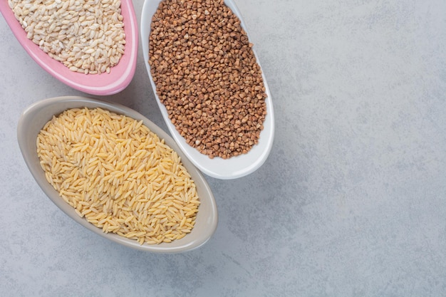 Three bowls with rice, wheat and buckwheat on marble surface