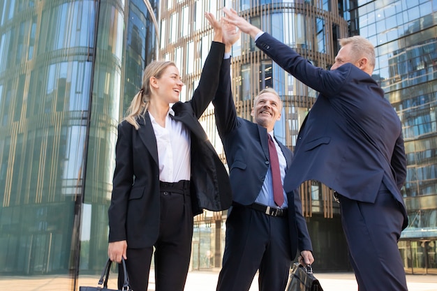 Free Photo three cheerful businesspeople giving five and smiling. confident happy colleagues celebrating successful deal together, standing outdoors and rising hand up. teamwork and partnership concept