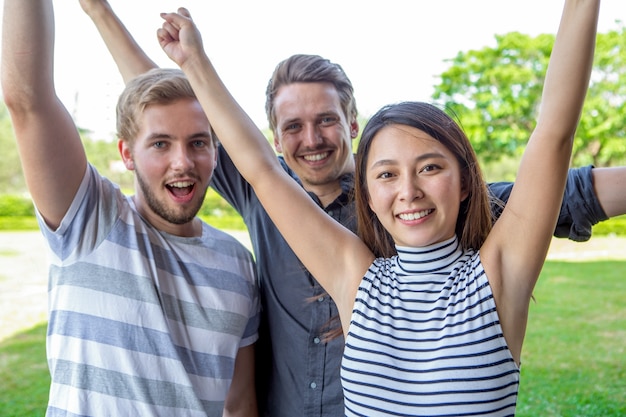 Free photo three cheerful multiethnic friends raising hands