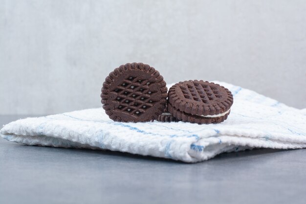 Three chocolate cookies lying on tablecloth.