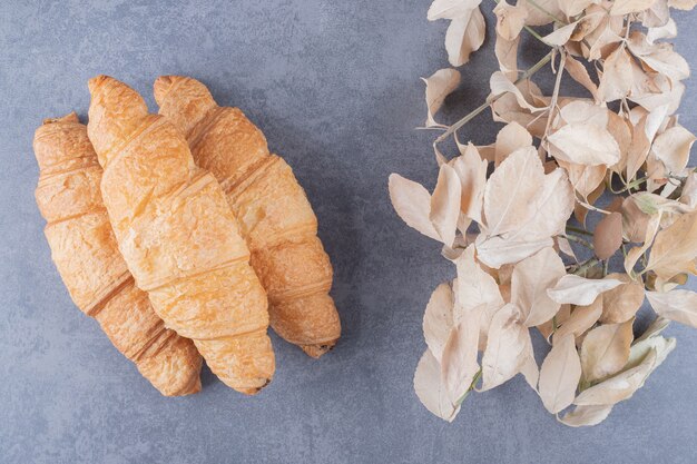 Three classic French croissant with decorative leaves over grey background.