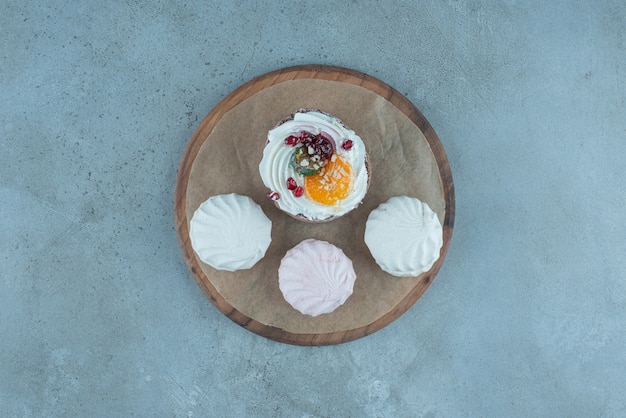 Free Photo three cookies and a cake on a wooden board on marble.