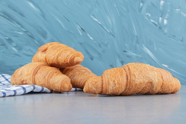 Three croissants stacked on the towel with a croissant on the marble background. High quality photo