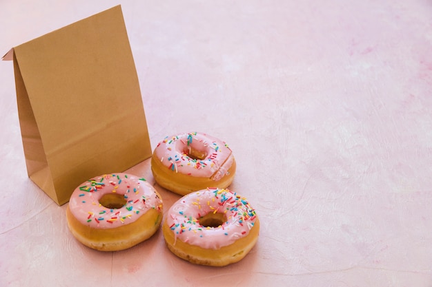 Three delicious donuts with parcel on pink background