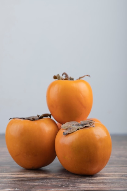 Free photo three delicious fuyu persimmons placed on wooden table