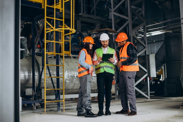 Three factory workers in safety hats discussing manufacture plan